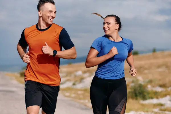スポーツウェアを着たカップルは 早朝のトレーニング中に美しい道に沿って走り 新鮮な空気を楽しみ 健康的なライフスタイルを維持します ストック写真