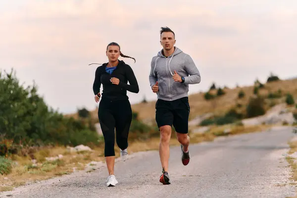 スポーツウェアを着たカップルは 早朝のトレーニング中に美しい道に沿って走り 新鮮な空気を楽しみ 健康的なライフスタイルを維持します ロイヤリティフリーのストック写真