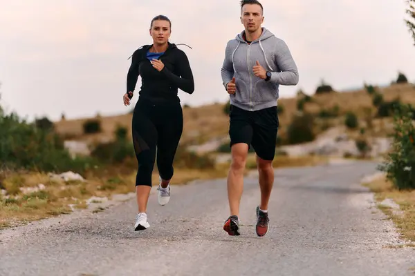 一对穿着运动服的夫妇在晨练时沿着风景秀丽的道路跑步 享受新鲜空气 保持健康的生活方式 图库图片