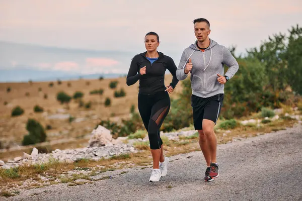 スポーツウェアを着たカップルは 早朝のトレーニング中に美しい道に沿って走り 新鮮な空気を楽しみ 健康的なライフスタイルを維持します ストックフォト