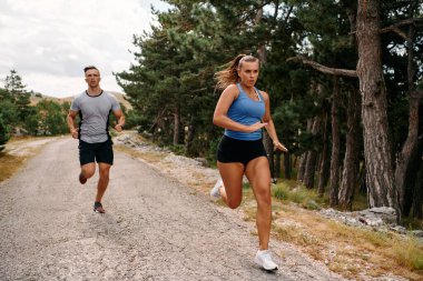A couple dressed in sportswear runs along a scenic road during an early morning workout, enjoying the fresh air and maintaining a healthy lifestyle. clipart