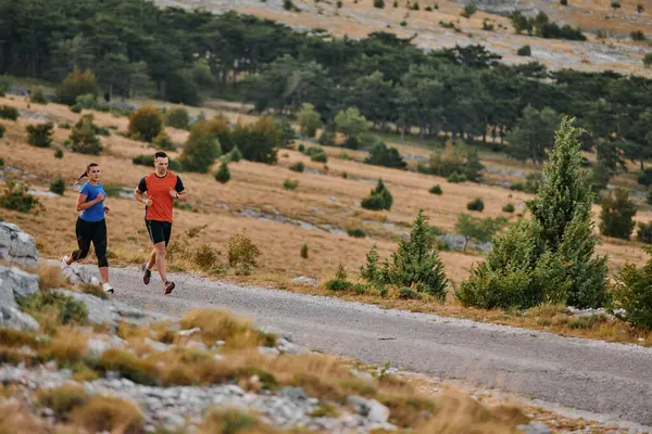 スポーツウェアを着たカップルは 早朝のトレーニング中に美しい道に沿って走り 新鮮な空気を楽しみ 健康的なライフスタイルを維持します ストック画像