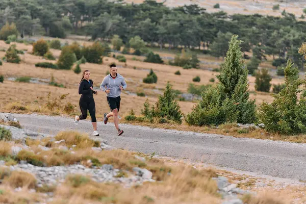 一对穿着运动服的夫妇在晨练时沿着风景秀丽的道路跑步 享受新鲜空气 保持健康的生活方式 图库图片