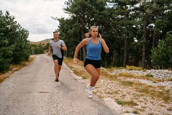 スポーツウェアを着たカップルは 早朝のトレーニング中に美しい道に沿って走り 新鮮な空気を楽しみ 健康的なライフスタイルを維持します ストック写真
