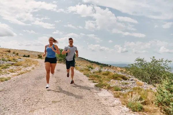 一对穿着运动服的夫妇在晨练时沿着风景秀丽的道路跑步 享受新鲜空气 保持健康的生活方式 图库照片