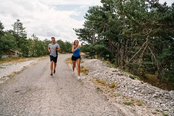 スポーツウェアを着たカップルは 早朝のトレーニング中に美しい道に沿って走り 新鮮な空気を楽しみ 健康的なライフスタイルを維持します ストックフォト