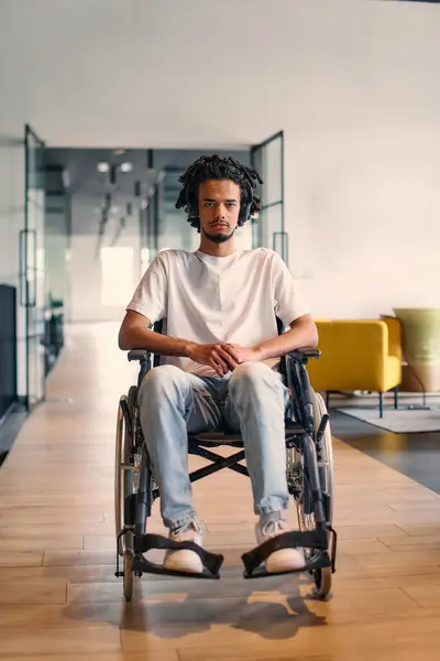 車椅子のアフリカ系アメリカ人の若い起業家は 現代のオフィス環境で彼のビジネス同僚に囲まれ 職場での多様性とコラボレーションを体現しています — ストック写真