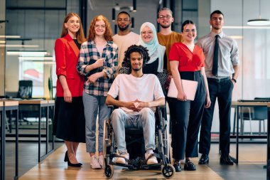 Modern bir girişimin cam kaplı ofisinde koridorda yürüyen bir grup genç iş adamı arasında tekerlekli sandalyedeki bir kişi ve tesettürlü bir kadın da var..