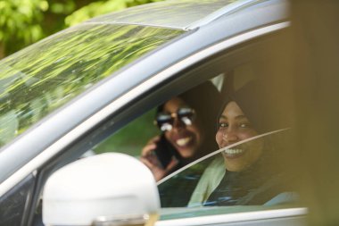 Başörtüsü takan iki Müslüman kadın, bir arabada seyahat ederken akıllı bir telefonla sohbet ediyorlar..