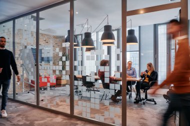 İş ortamının hareketli koşuşturmasında, bir grup genç iş adamı ofislerinin yanındaki koridorda yürürken, meslektaşları içeride iş birliği yaparak,