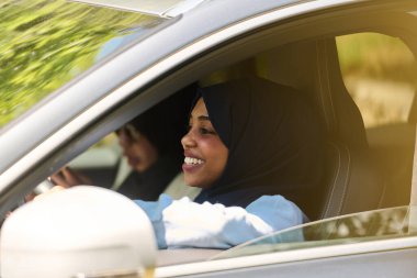Başörtüsü takan iki Müslüman kadın, bir arabada seyahat ederken akıllı bir telefonla sohbet ediyorlar..