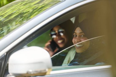 Başörtüsü takan iki Müslüman kadın, bir arabada seyahat ederken akıllı bir telefonla sohbet ediyorlar..