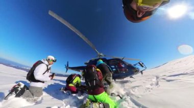 Helikopter kayakçıları dağın yamacına bıraktı ve bir kar bulutu kaldırarak uçtu. Güzel bir kış güneşli bir günde bir grup arkadaş taze toz karda serbest kayak yapmak için helikoptere biniyor.