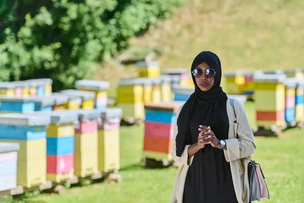 stock image African American Muslim woman in hijab explores natural bee farms for honey production, blending tradition with sustainability in the serene countryside. 