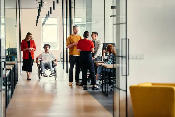 stock image A diverse group of young professionals, including businesswomen and an African-American entrepreneur in a wheelchair, engage in collaborative discussion on various business projects in a modern