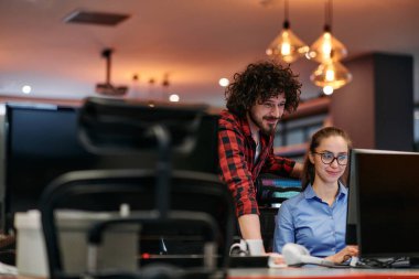 İş arkadaşları, bir erkek ve bir kadın, bilgisayar monitörüne dikkatle bakarken iş stratejilerini tartışır, işbirliği ve yenilikleri ön plana çıkarırlar.. 