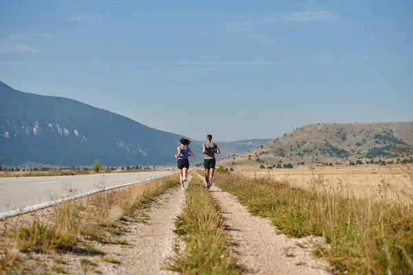 stock image A couple runs through a sun-dappled road, their bodies strong and healthy, their love for each other and the outdoors evident in every stride. 