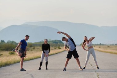 Kararlı bir grup sporcu koşularından önce kolektif bir esneme oturumuna katılıyor, takım çalışmasını teşvik ediyor ve fitness hedeflerini gerçekleştirmek için hazırlık yapıyorlar..