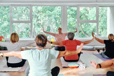 Bir grup son sınıf öğrencisi, güneş alan bir alanda eğitmenin rehberliğinde boyun, sırt ve bacak esnetme gibi çeşitli yoga egzersizleri yaparak refahı ve uyumu sağlıyorlar.. 