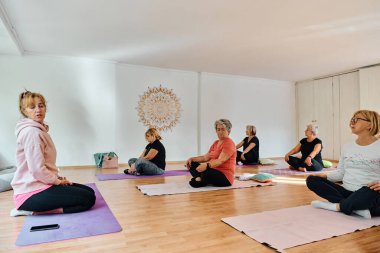 Bir grup son sınıf öğrencisi, güneş alan bir alanda eğitmenin rehberliğinde boyun, sırt ve bacak esnetme gibi çeşitli yoga egzersizleri yaparak refahı ve uyumu sağlıyorlar.. 