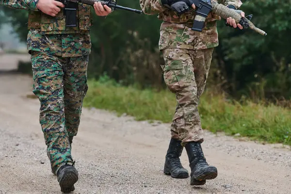 stock image Close up photo, the resilient legs of elite soldiers, clad in camouflage boots, stride purposefully along a hazardous forest path as they embark on a high-stakes military mission. 