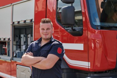 Kendine güvenen itfaiyeci, çapraz kollarla ayakta duruyor, dayanıklılık ve hazırlık yayıyor, modern bir itfaiye aracının yanında acil durumlara cevap vermeye hazır, ateşin kahramanlığını ve gücünü gösteriyor.