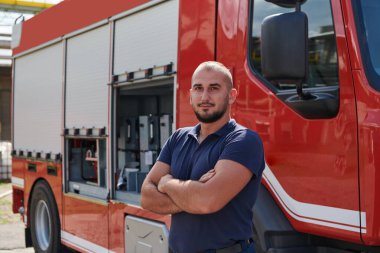 Kendine güvenen itfaiyeci, çapraz kollarla ayakta duruyor, dayanıklılık ve hazırlık yayıyor, modern bir itfaiye aracının yanında acil durumlara cevap vermeye hazır, ateşin kahramanlığını ve gücünü gösteriyor.