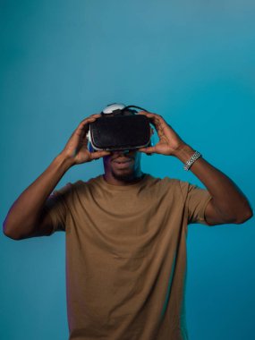 Gelecekteki bir görüntüde, Afrikalı Amerikalı bir adam, VR gözlükleriyle süslenmiş, çarpıcı bir mavi arkaplana karşı izole bir şekilde duruyor ve bu da onu son teknoloji sanal gerçeklik deneyimine taşıyor.