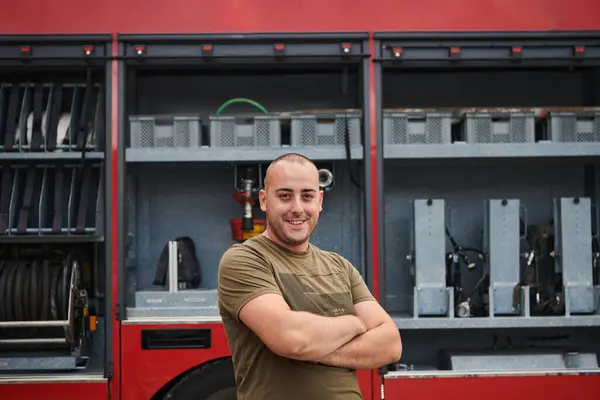 stock image Confident firefighter stands with crossed arms, exuding resilience and preparedness, ready to respond to emergencies alongside a modern fire truck, showcasing the heroism and strength of the fire