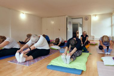 Bir grup son sınıf öğrencisi, güneş alan bir alanda eğitmenin rehberliğinde boyun, sırt ve bacak esnetme gibi çeşitli yoga egzersizleri yaparak refahı ve uyumu sağlıyorlar.. 