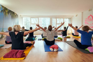 Bir grup son sınıf öğrencisi, güneş alan bir alanda eğitmenin rehberliğinde boyun, sırt ve bacak esnetme gibi çeşitli yoga egzersizleri yaparak refahı ve uyumu sağlıyorlar.. 
