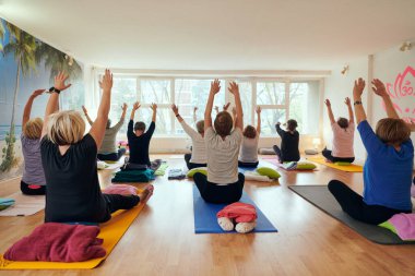 Bir grup son sınıf öğrencisi, güneş alan bir alanda eğitmenin rehberliğinde boyun, sırt ve bacak esnetme gibi çeşitli yoga egzersizleri yaparak refahı ve uyumu sağlıyorlar.. 