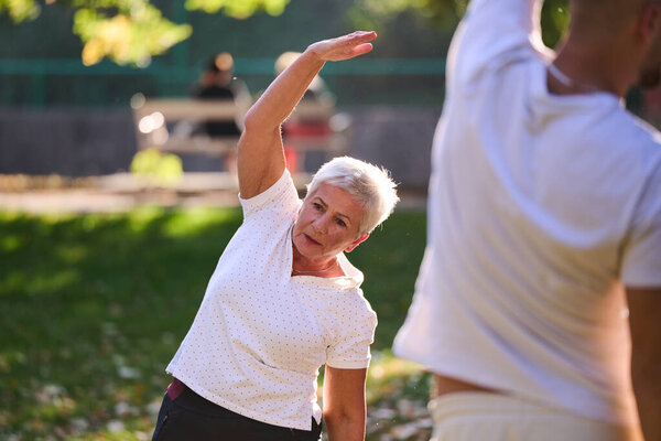 A group of seniors follows a trainer, engaging in outdoor exercises in the park, as they collectively strive to maintain vitality and well-being, embracing an active and health-conscious lifestyle in