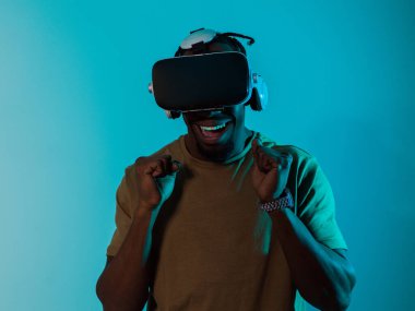 Afro-Amerikalı bir adam, VR gözlüklerini kullanarak çarpıcı bir mavi arka plana karşı izole ve yoğun bir atmosfer yaratarak heyecan verici bir korku oyunu deneyimine daldı..