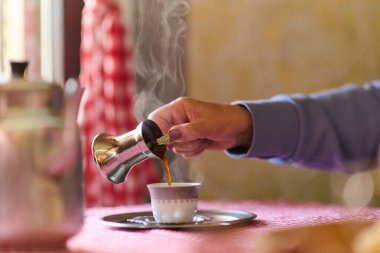 Yaşlı bir kadın, kırsal evinin verandasında bir fincan kahvenin tadını çıkarırken, doğanın basitliği ve derin düşüncelere daldığı anlarda teselli buluyor.. 