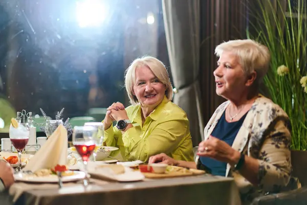 Stock image Elderly friends share a delightful dinner, filled with laughter, joy, and the warmth of enduring friendship, epitomizing the timeless pleasure of companionship in a contemporary setting. 