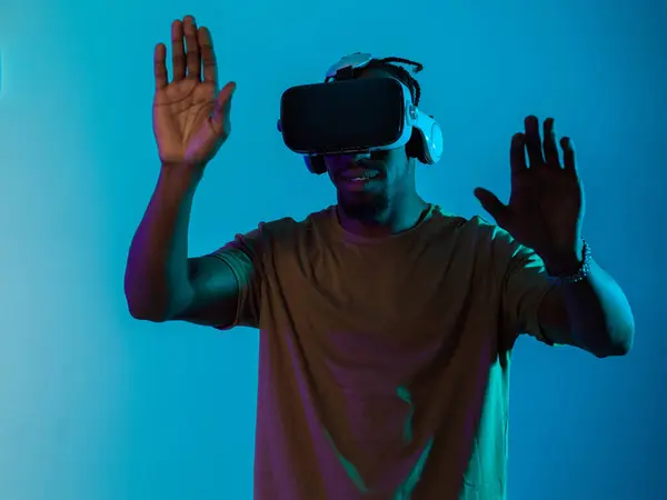 Stock image Immersed in a digital realm, an African American man navigates the virtual landscape with a VR goggles, using tactile gestures to interact with virtual objects, showcasing a harmonious blend of