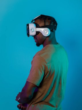 Gelecekteki bir görüntüde, Afrikalı Amerikalı bir adam, VR gözlükleriyle süslenmiş, çarpıcı bir mavi arkaplana karşı izole bir şekilde duruyor ve bu da onu son teknoloji sanal gerçeklik deneyimine taşıyor.