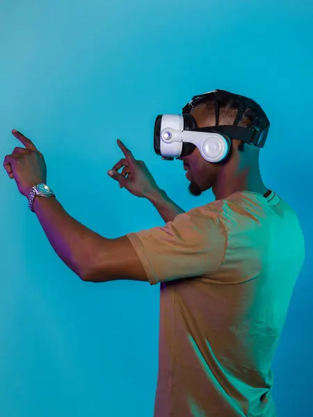 Stock image Immersed in a digital realm, an African American man navigates the virtual landscape with a VR goggles, using tactile gestures to interact with virtual objects, showcasing a harmonious blend of