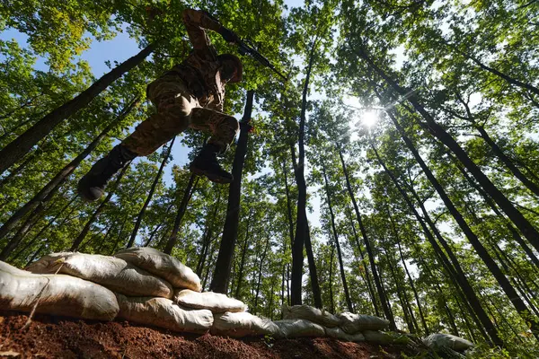 stock image An elite soldier adeptly clears military barriers in the perilous wooded terrain, showcasing tactical skill and agility during specialized training. 