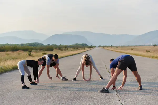 stock image A determined group of athletes engage in a collective stretching session before their run, fostering teamwork and preparation in pursuit of their fitness goals.