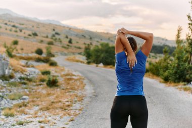 Kararlı bir dişi atlet, engebeli dağ arazilerinde nefes kesici kaya manzaralarıyla çevrili yorucu bir koşudan sonra kaslarını esnetir.. 