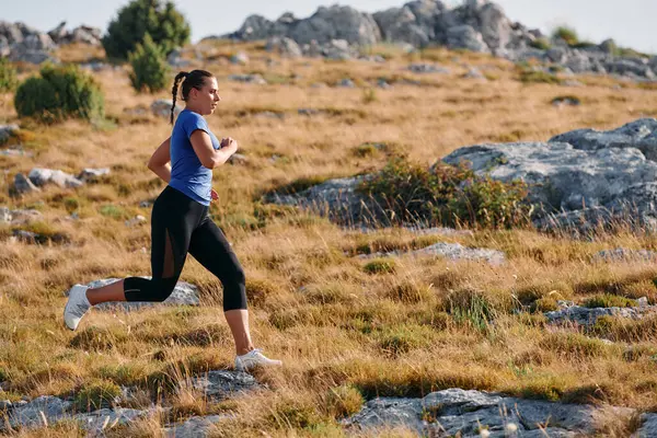 stock image A determined female athlete runs through a forest trail at sunrise, surrounded by breathtaking natural beauty and vibrant greenery. 