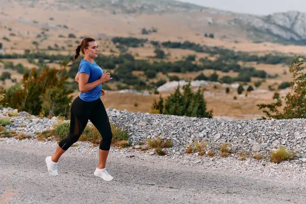 stock image A determined female athlete runs through a forest trail at sunrise, surrounded by breathtaking natural beauty and vibrant greenery. 