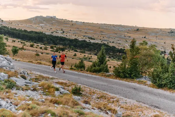 stock image A couple dressed in sportswear runs along a scenic road during an early morning workout, enjoying the fresh air and maintaining a healthy lifestyle.