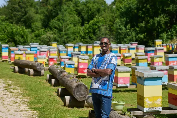 stock image  African American teenager clad in traditional Sudanese attire explores small beekeeping businesses amidst the beauty of nature