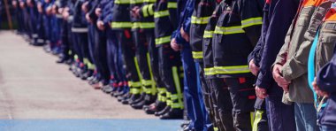 Bir grup itfaiyeci sıraya girmiş, bayrağı selamlıyor, dayanışma içinde alkışlıyor, yoğun antrenman için hazırlanıyor, servis ve takım çalışmasına olan sarsılmaz bağlılıklarını sergiliyorlar.