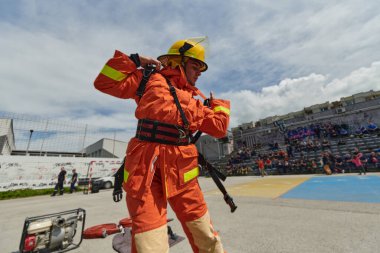 Senkronize takım çalışmasının dinamik bir gösterisinde itfaiyeciler itfaiye hortumlarını titizlikle taşımak, bağlamak ve yerleştirmek için çabalarlar. Yoğun eğitimlerini ve meydan okumaya hazır olduklarını gösterirler.