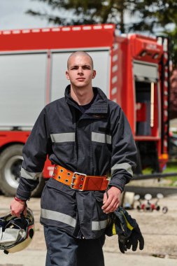 Profesyonel kıyafetlerle süslenmiş bir itfaiyeci, yorucu bir itfaiyecilik eğitiminden sonra itfaiye aracının yanında güven içinde durur. 