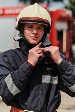 Profesyonel kıyafetlerle süslenmiş bir itfaiyeci, yorucu bir itfaiyecilik eğitiminden sonra itfaiye aracının yanında güven içinde durur. 